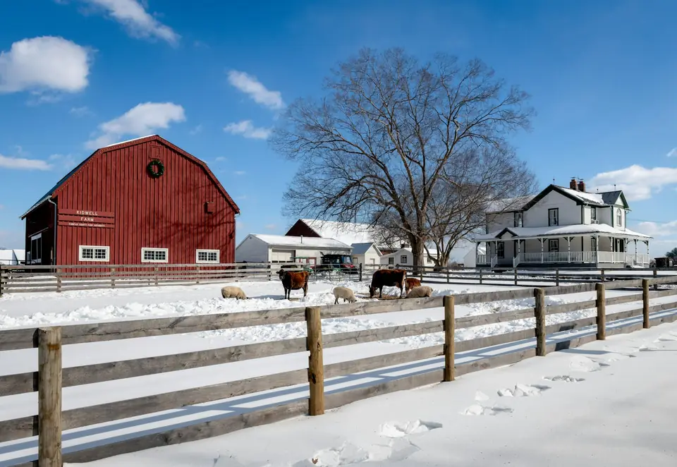 Red barn and farmhouse behind a fence on a snowy winter day