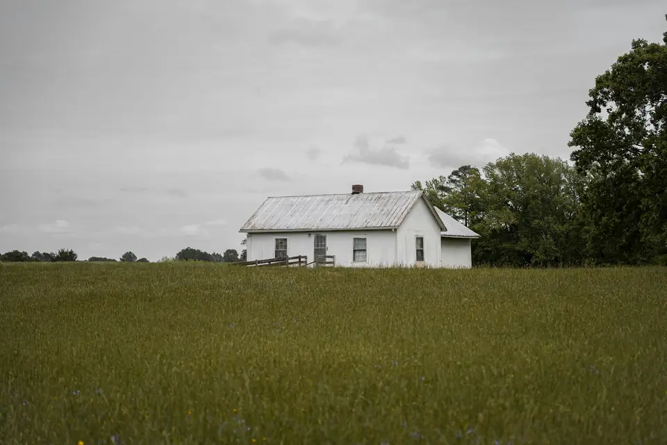White farmhouse at the edge of a green field under an overcast sky